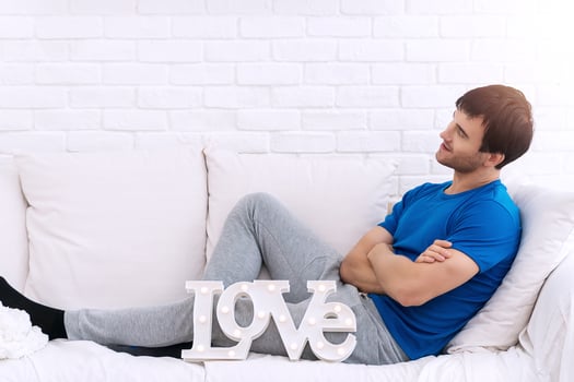 Handsome young man arms crossed sitting on white sofa with LOVE alphabet looking at something. Love and Valentine's Day concept. photo