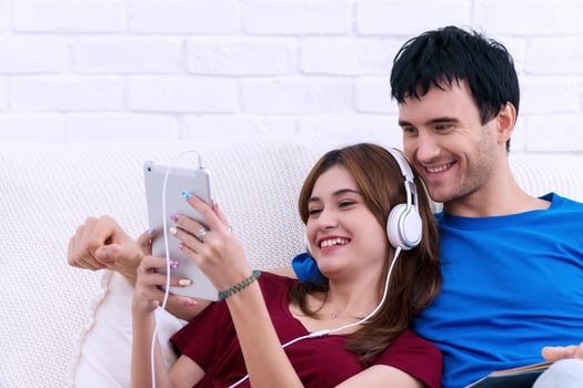 Happy young married couple relaxing together at home with the wife lying back against her husband as she listen to music on tablet. photo