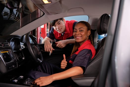 Young Black female automotive mechanic technician and partner check maintenance list in car interior at garage with smiles. Vehicle service fix and repair works, industrial occupation business jobs. photo