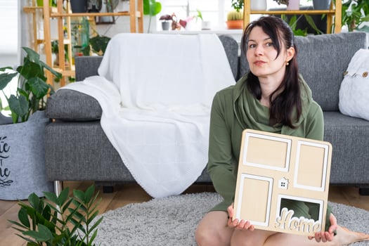 Happy woman in house holds in hands photo frame with figure at home template and key in interior. Dream house project, real estate purchase, insurance, mortgage, rent, reservation