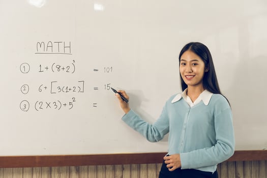 Asian female teacher is teaching students at the classroom while pointing at numbers on the white board. photo