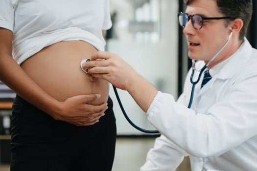 Pregnant african woman has appointment with doctor at clinic. Male gynaecologist OB GYN medic specialist with stethoscope listens to baby's heartbeat in mother's belly. photo