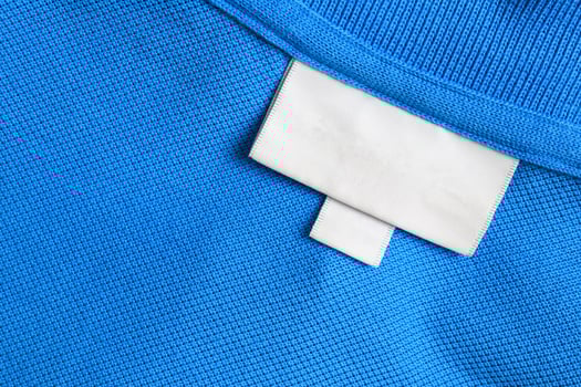 Blank white laundry care clothes label on blue shirt fabric texture background photo
