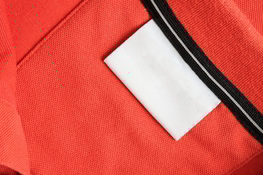 Blank white laundry care clothes label on orange shirt fabric texture background photo