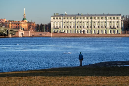 Teenager looks over the blue river of Neva in St. Petersburg Russia. Back view. Architecture of embankments of rivers and canals of St. Petersburg. photo