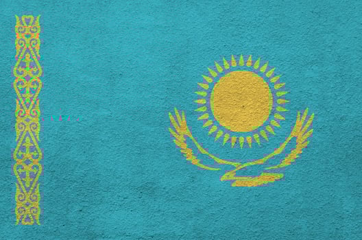 Kazakhstan flag depicted in bright paint colors on old relief plastering wall. Textured banner on rough background photo