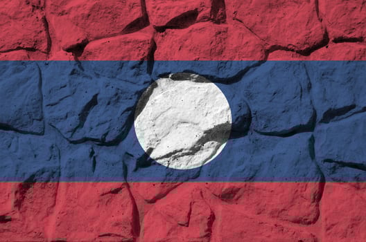 Laos flag depicted in paint colors on old stone wall closeup. Textured banner on rock wall background photo