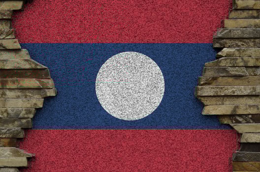Laos flag depicted in paint colors on old stone wall closeup. Textured banner on rock wall background photo