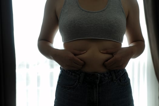 Close up of a belly with scar from c-section and abdominal fat. Women's health. A woman dressed up in sportswear demonstrating her imperfect body after a childbirth with nursery on the background. photo
