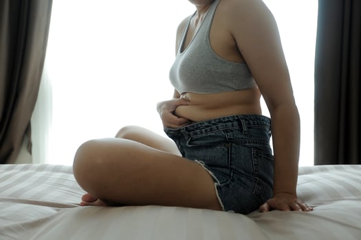 Close up of a belly with scar from c-section and abdominal fat. Women's health. A woman dressed up in sportswear demonstrating her imperfect body after a childbirth with nursery on the background. photo