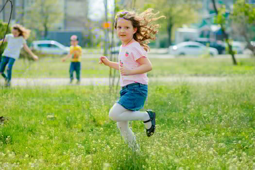beautiful little girl with developing hair walks in street violating quarantine of coronavirus. girl in pink T-shirt runs across green field. girl plays active games in nature in summer or spring. photo