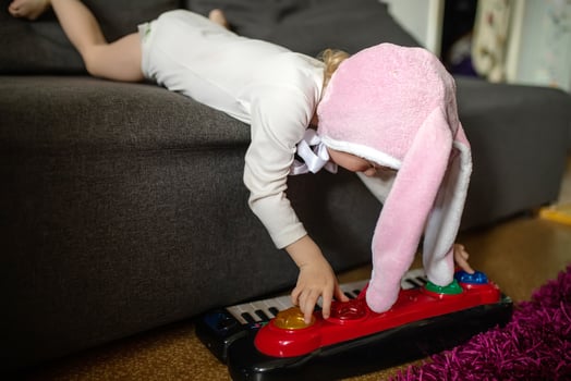 Child playing on synthesizer. A little girl lies on a gray couch and plays with a children's piano. Early music education for little kids, children at school, learning music instruments photo