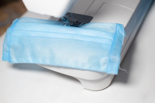 Three-layer medical protective mask at time of sewing on electric sewing machine. Helping doctors. Making anti-virus protections during coronavirus pandemic. photo