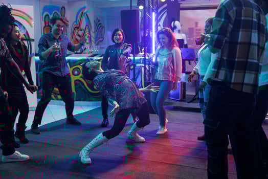 Friends watching woman dancing in nightclub, laughing while attending disco party. Diverse happy people crowd enjoying night discotheque on dancefloor with spotlights in club photo