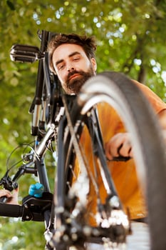 Healthy vibrant caucasian man is seen outdoors doing annual upkeeping and maintenance of modern bicycle. Active young male cyclist checking and ensuring functioning of bike pedal. photo