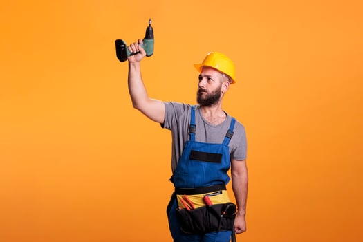 Young carpenter working wtih electric power drill tool, wearing overalls and holding drilling gun. Handyman contractor using cordless drill to work on renovation and refurbishment. photo