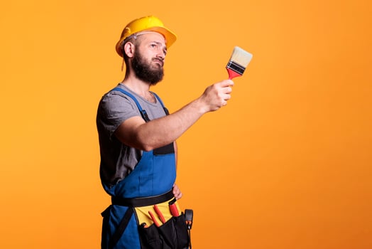 Male contractor holding paintbrush to color walls, working on refurbishment project and painting with tools. Construction worker painter doing renovation work with brush and paint. photo