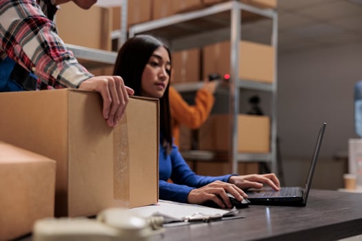 Warehouse workers preparing parcel for delivery and analyzing orders on laptop while working at storage room desk. Storehouse employees cooperating to manage cardboard box shipping photo