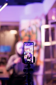 Anonymous criminal recording malicious activity on smartphone screen. Hacker with hidden identity live streaming threat message to victim on mobile phone display in hideout photo