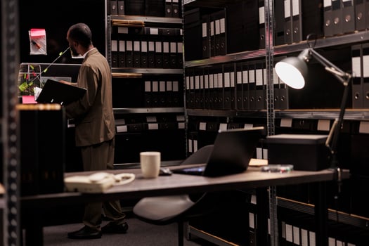 Police investigator standing near detective board analyzing clues scheme. Young law enforcement professional holding folder with csi report and looking at evidence map hanging on wall photo