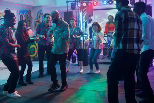 Young clubbers dancing at discotheque in nightclub and partying together. Diverse people crowd moving on dancefloor while attending party with live music show in club at night photo