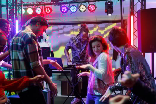 People dancing while dj performing live on stage at nightclub disco party. Diverse men and women crowd having fun and moving on dancefloor during musician concert at club photo