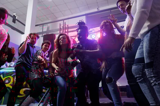 Young people dancing and jumping together on dancefloor in nightclub. Diverse men and women friends partying and clubbing at club party while enjoying nightlife entertainment photo