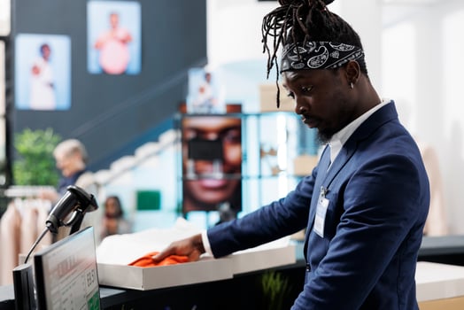 African american employee standing at cash register, preparing customer packages. Showroom worker putting fashionable clothes in carton boxes, working in shopping centre. Fashion concept photo