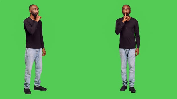 Young adult showing hush sign on camera, expressing privacy and silence in studio. Private person doing mute symbol and being confidential, keeping secret over full body green screen. photo