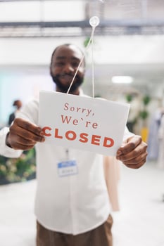 Smiling african american man hanging closed sign in window of fashion boutique, noticing about work day end. Clothes retail shopping mall cheerful assistant putting information sign on door photo