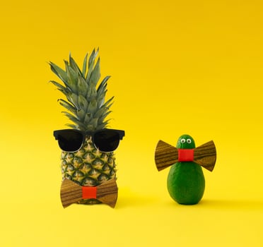 Creative and funny composition made of fresh pineapple and avocado with sunglasses and wooden bow tie on yellow background. Minimal exotic fruit concept. Trendy food idea. Tropical fruit aesthetic. photo