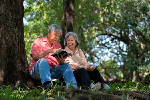 Happy Asian old senior couple with gray hair reading a book outside in park. Concept of happy elderly after retirement and good health photo