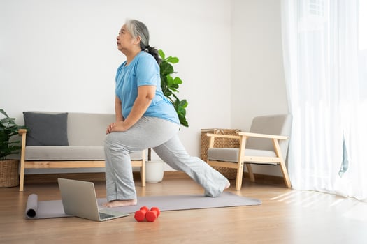 Senior Asian woman watching online courses on a laptop while exercising in the living room at home. Old woman stretching exercises in the living room at home, Concept of workout training online. photo