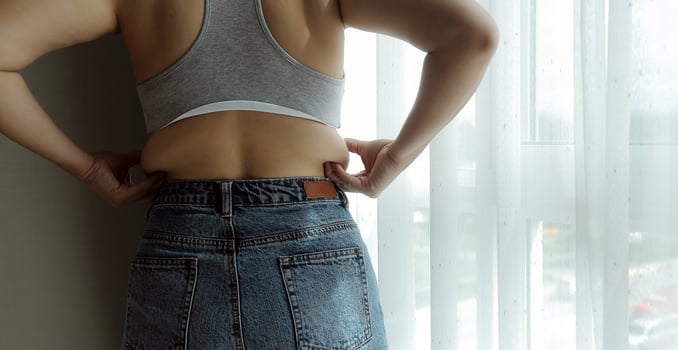 Close up of a belly with scar from c-section and abdominal fat. Women's health. A woman dressed up in sportswear demonstrating her imperfect body after a childbirth with nursery on the background. photo