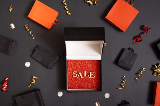 Black friday sale concept. Sale text in black gift box and shopping bags with festive decorations on black background flat lay, top view. photo