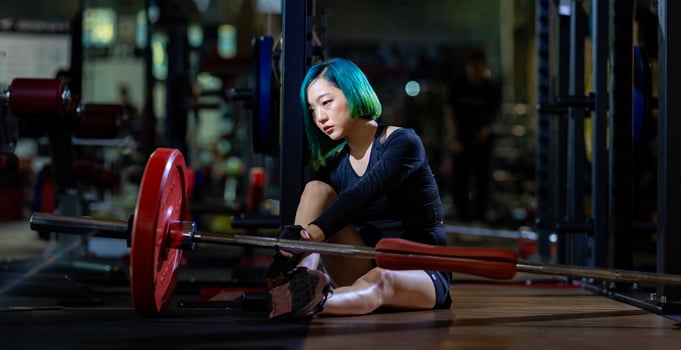 Asian woman is facing overtraining syndrome after weight training workout inside gym with dark background for exercising and fitness concept photo