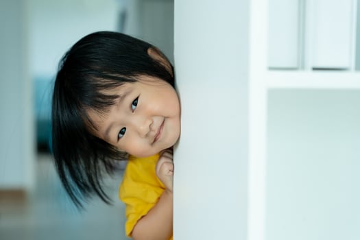 little asian children kid playing hide and seek standing next wall house, Adorable child having fun in the home. happy family have fun with kids, activity, learning, activity, game, meditation photo