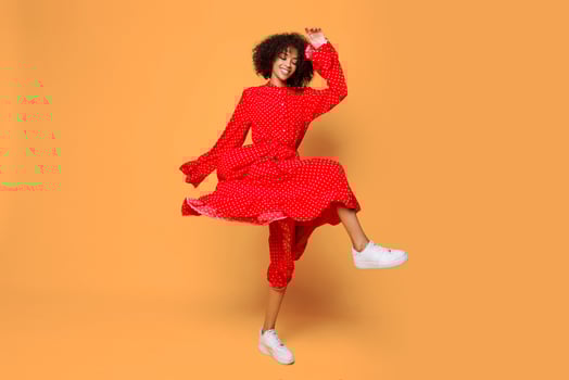 Dreamy mood. Stylish African girl dancing and jumping over orange background. Wearing red vintage dress . Shopping and fashion. photo