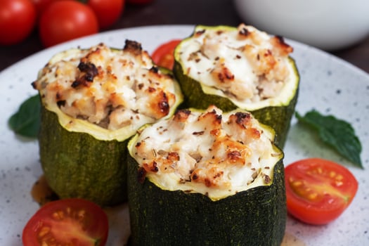 Baked stuffed zucchini columns with minced chicken and vegetables on a plate. Dark wooden background. photo