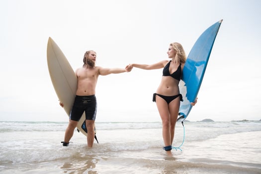 Couple of surfers holding hands and looking at each other on beach photo