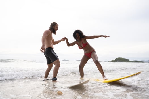 Couple surfing on the beach having fun and balancing on the surfboard photo