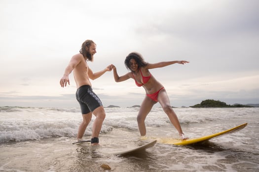Couple surfing on the beach having fun and balancing on the surfboard photo