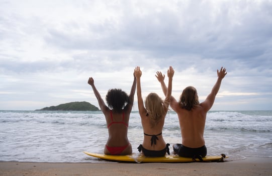 Rear view of three friends sitting on surfboard and looking at sea photo