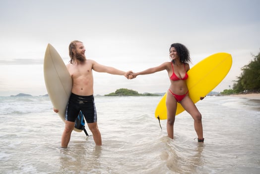 Couple of surfers holding hands and looking at each other on beach photo