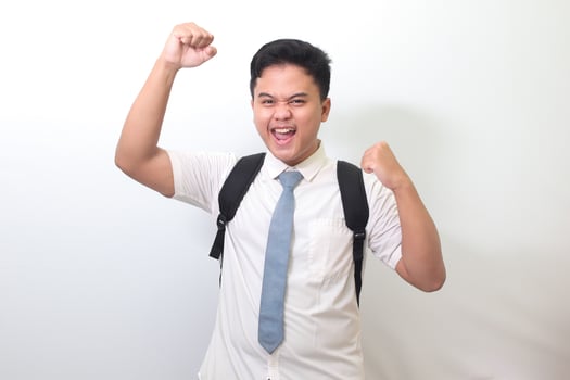 Indonesian senior high school student wearing white shirt uniform with gray tie raising his fist, celebrating success. Winning a competition concept. Isolated image on white background photo