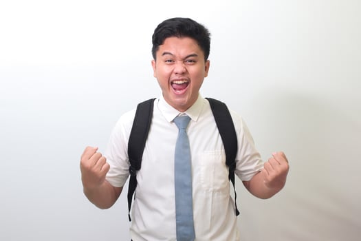 Indonesian senior high school student wearing white shirt uniform with gray tie raising his fist, celebrating success. Winning a competition concept. Isolated image on white background photo