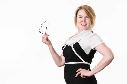 Smiling business lady in black-white dress holding glasses in bent arm, other hand placed on waist photo