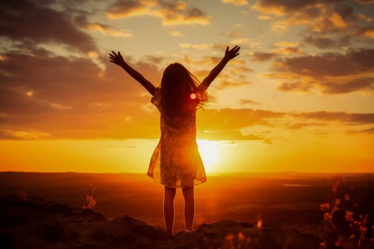 Preteen girl silhouette with raised hand over sunset sky embracing nature photo
