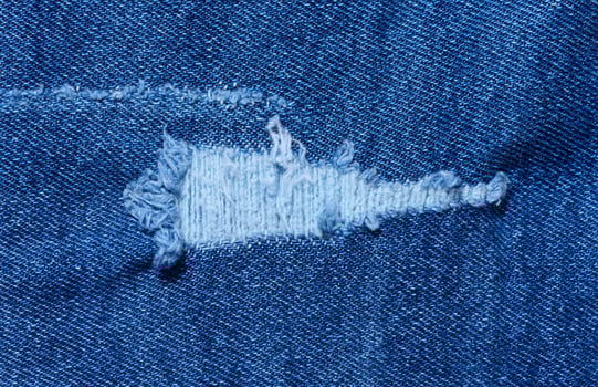 Fragment of blue jeans fabric with a hole, full frame, close up photo