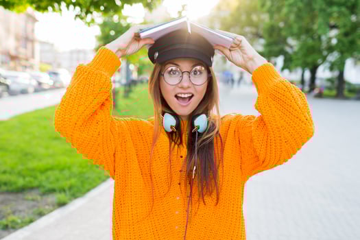 Happy student girl  with a book on her  head having fun outdoor after lessons. photo